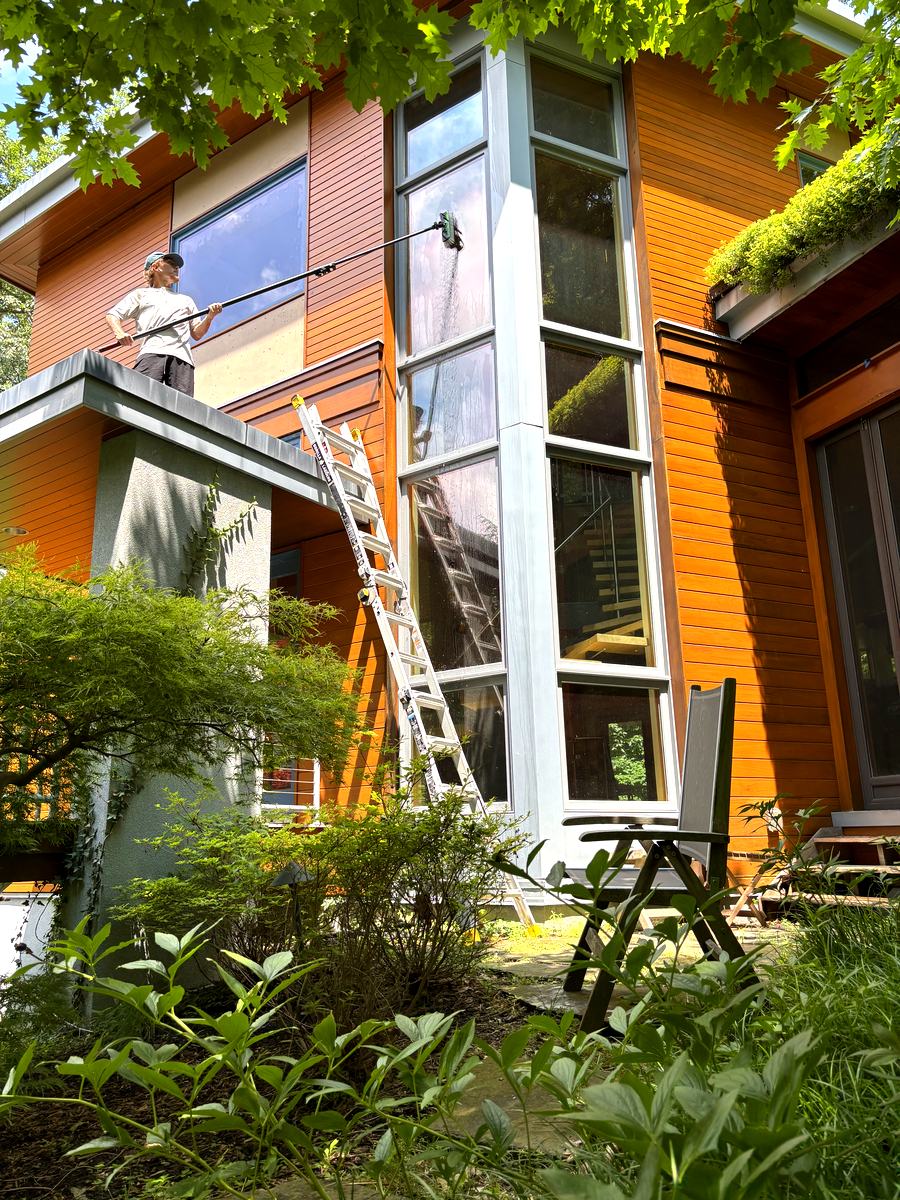 Window washing a tall glass corner on a modern wooded-lot home